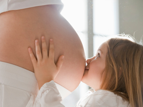 Girl kissing pregnant mother's belly, side view
